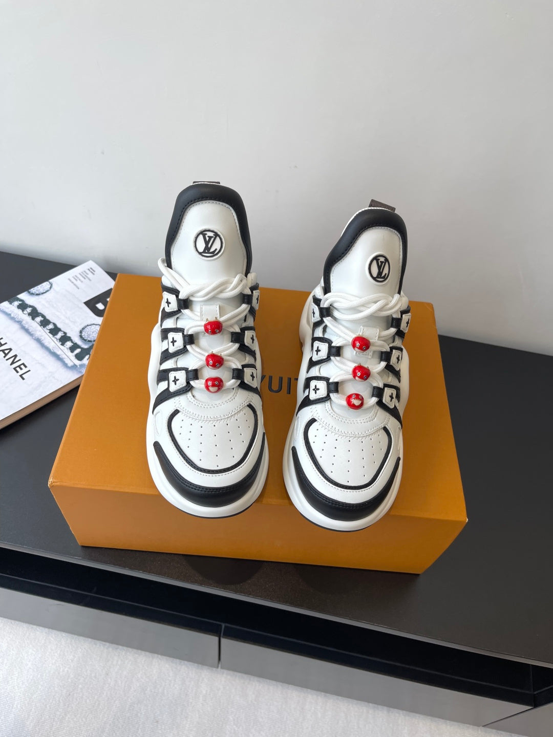 White and black low-top sneakers with black logo details and red beaded laces
