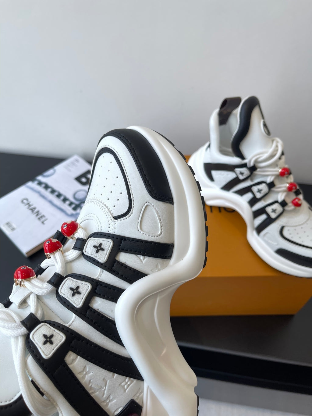 White and black sneaker side view with LV emblem and red beaded lace details