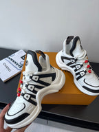 Pair of white and black sneakers with black strap details and red beaded laces
