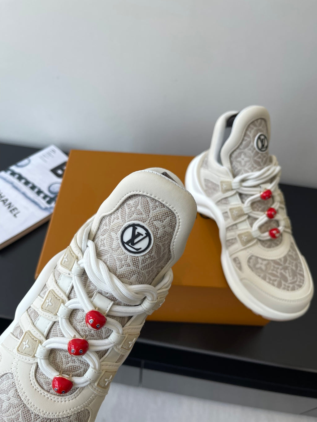Louis Vuitton low-top sneakers close-up, off-white with round LV patch and red lace beads