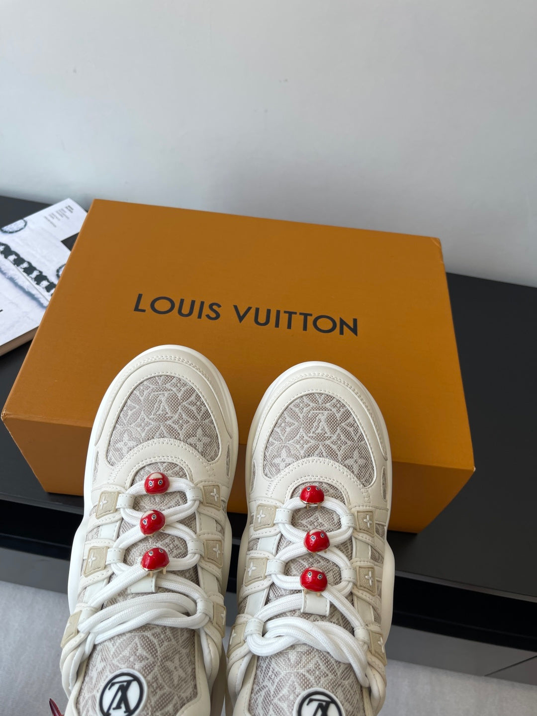 Louis Vuitton low-top sneakers on display, off-white with beige monogram uppers and red laces