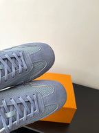 Light-blue lace-up sneakers with suede and mesh panels, shown on an orange box