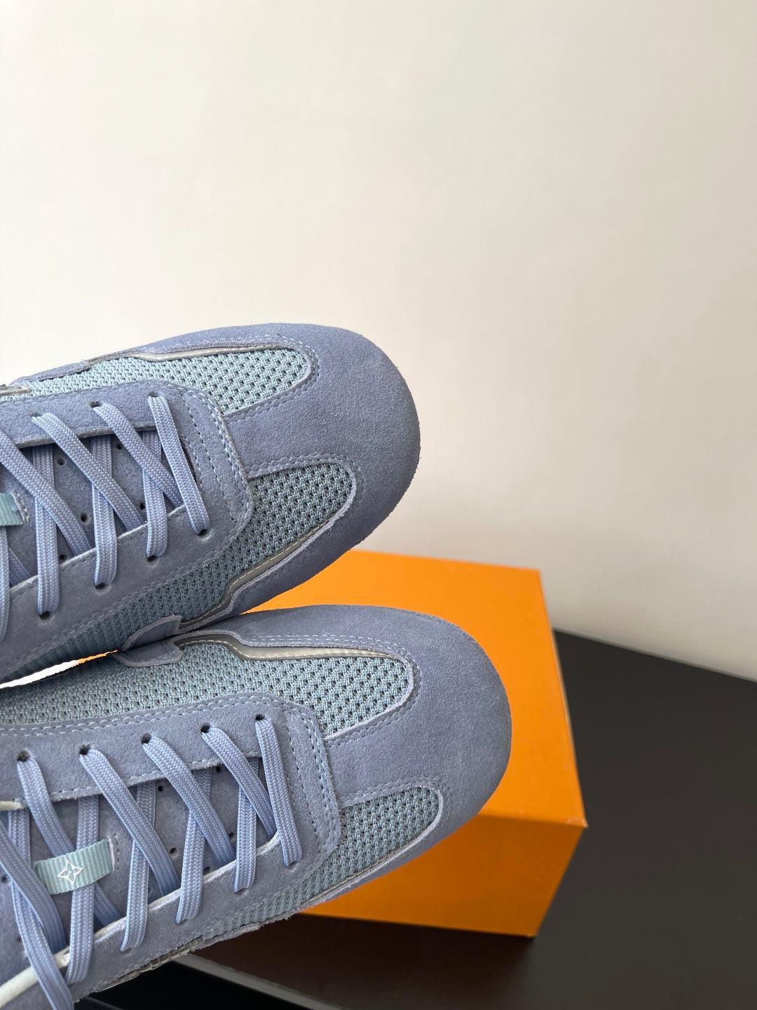 Light-blue lace-up sneakers with suede and mesh panels, shown on an orange box