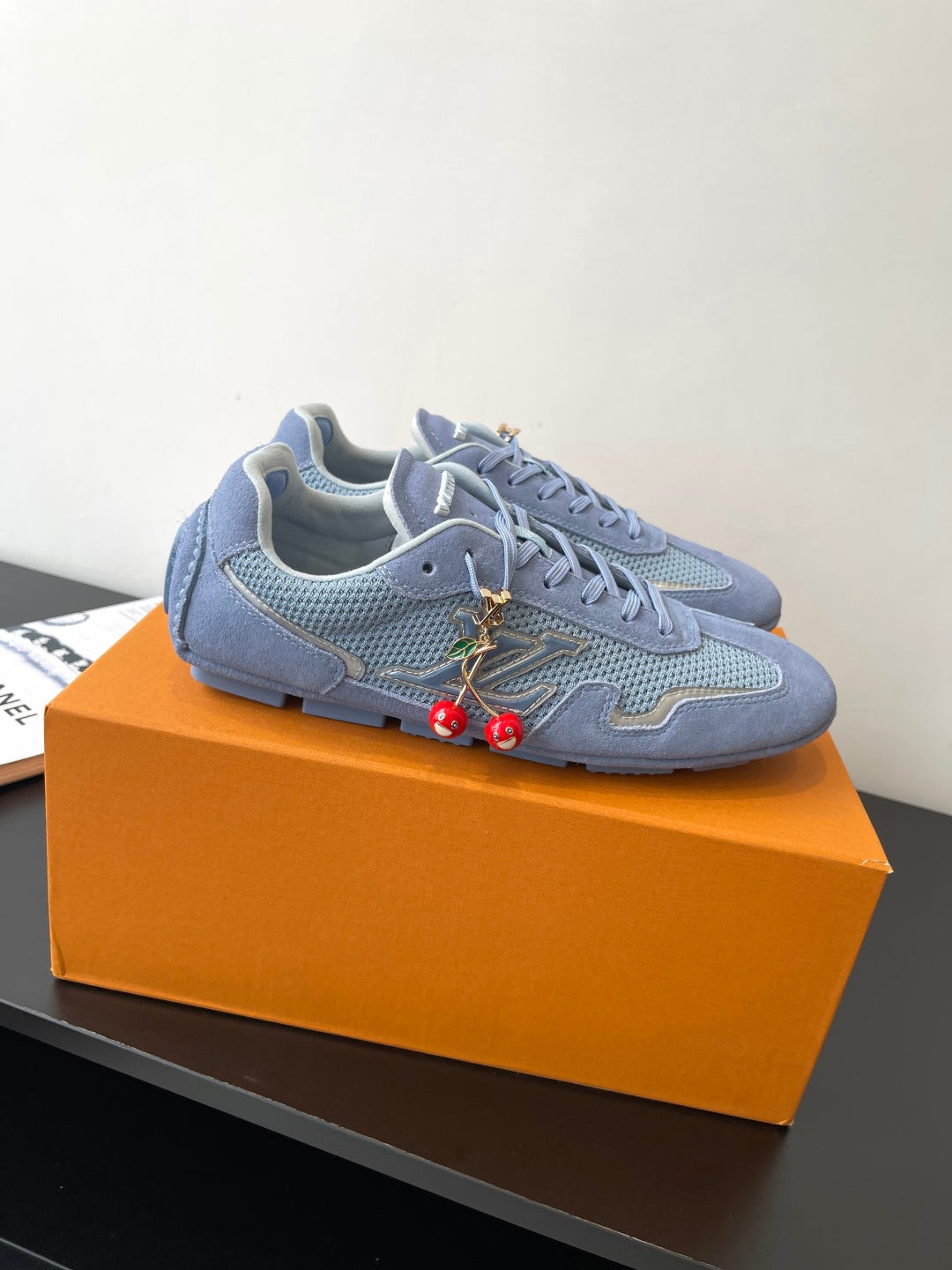 Light-blue lace-up sneakers with textured side panels, decorative laces, and red charm accents