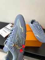 Light-blue lace-up sneakers with gold-and-green embroidered side detail and red charms