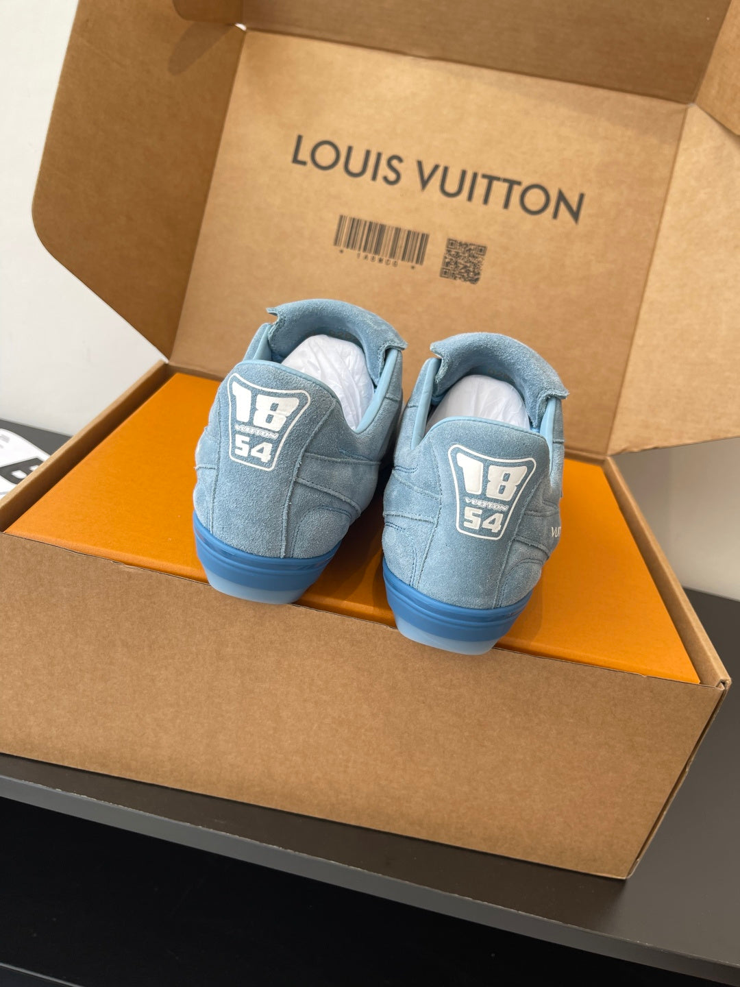 Light blue sneakers with rear logo patches, pair shown in open gift box