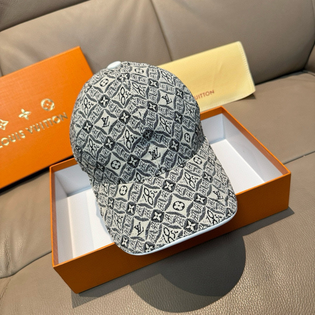 Monogram-pattern baseball cap in dark gray/black with curved brim, displayed on box.
