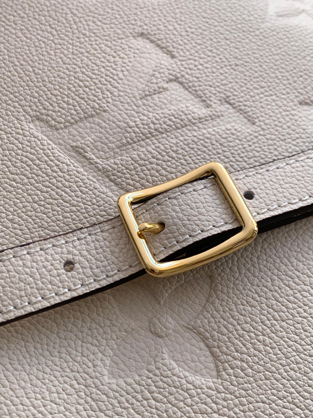 Louis Vuitton leather strap with gold-tone buckle on light beige pebble-grain material