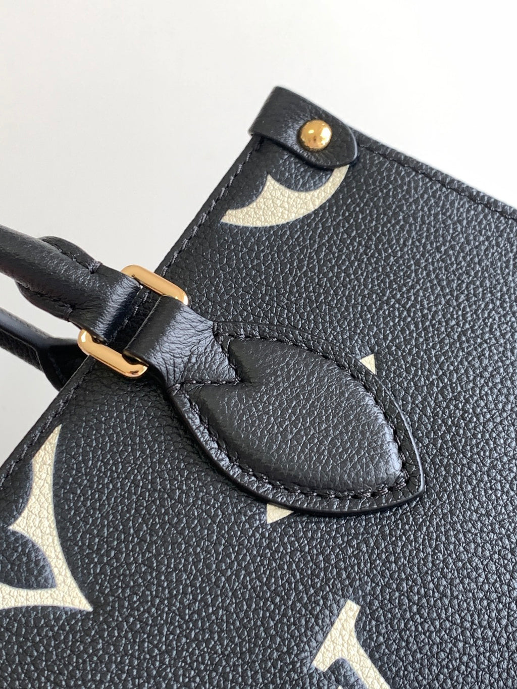 Louis Vuitton bag strap hardware and leather patch close-up on dark textured exterior