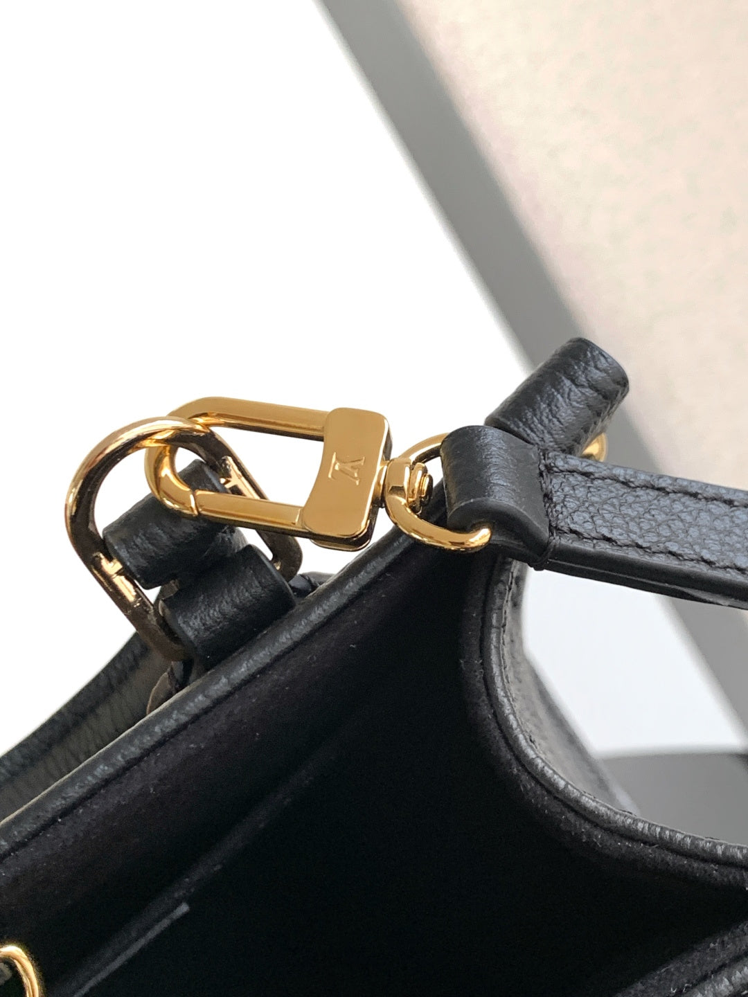 Black leather bag corner with gold-tone D-ring hardware and strap attachment