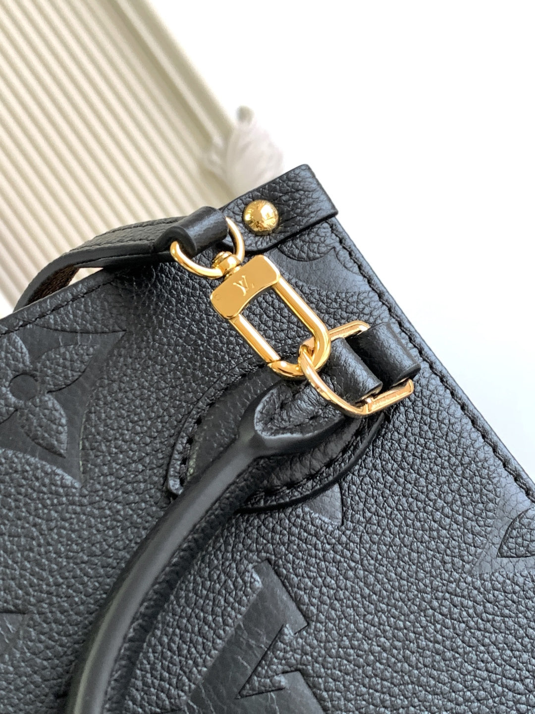 Black leather bag front flap with gold-tone clasp and embossed monogram
