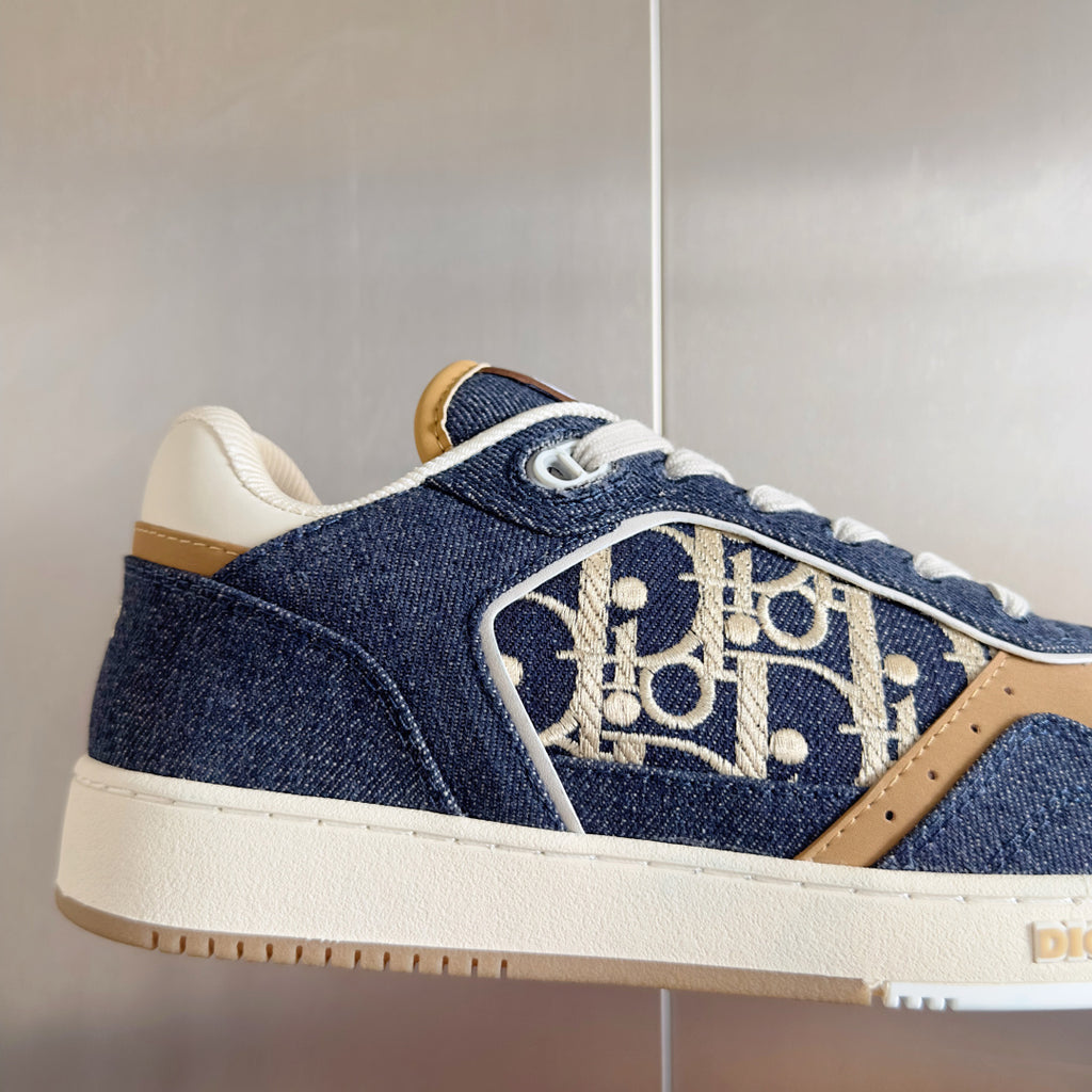 Unisex sneaker close-up: blue denim side panel with gold logo print, white sole