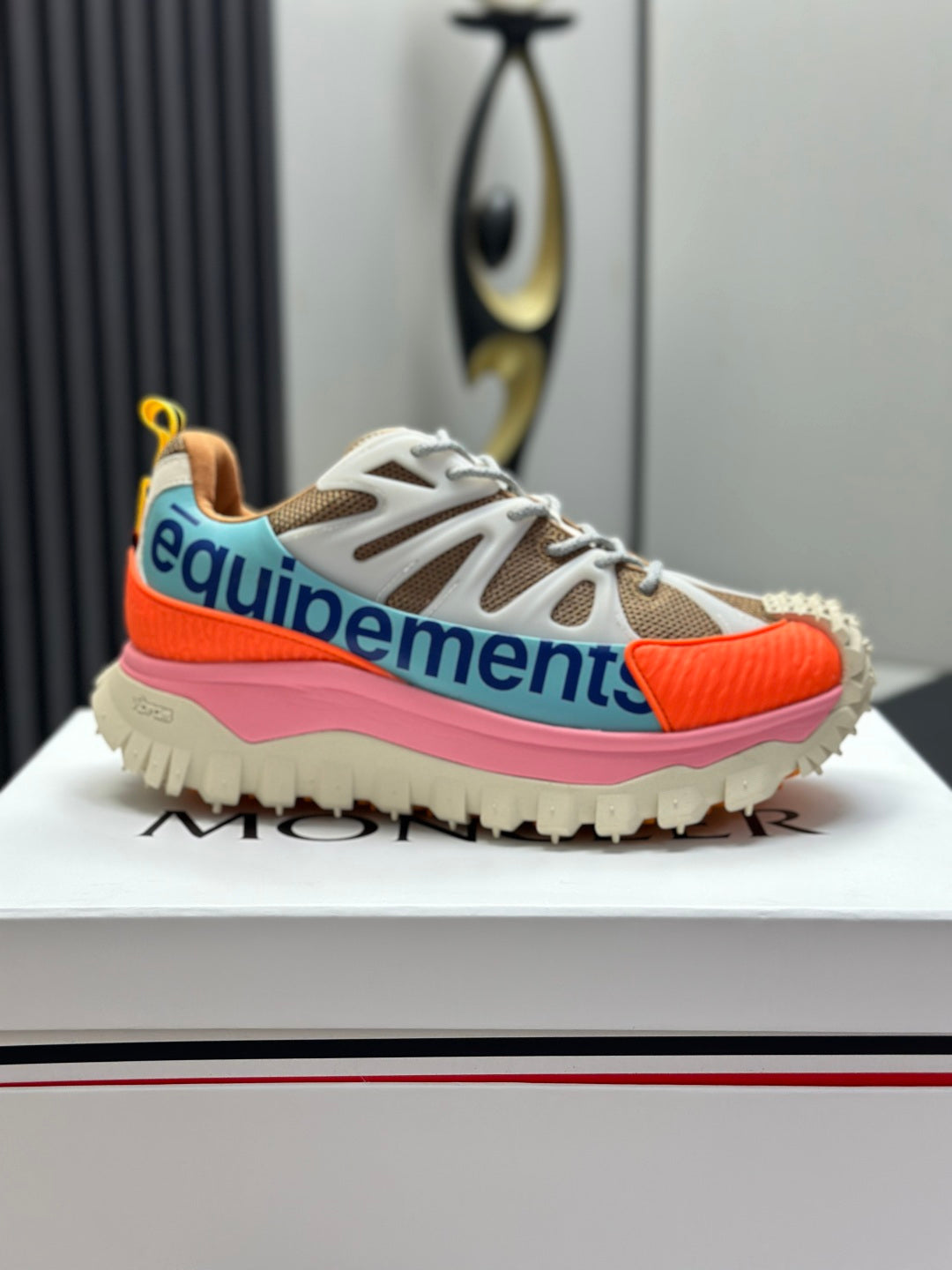 Moncler trail sneaker side view, white laces with orange toe panel, pink midsole, blue accent