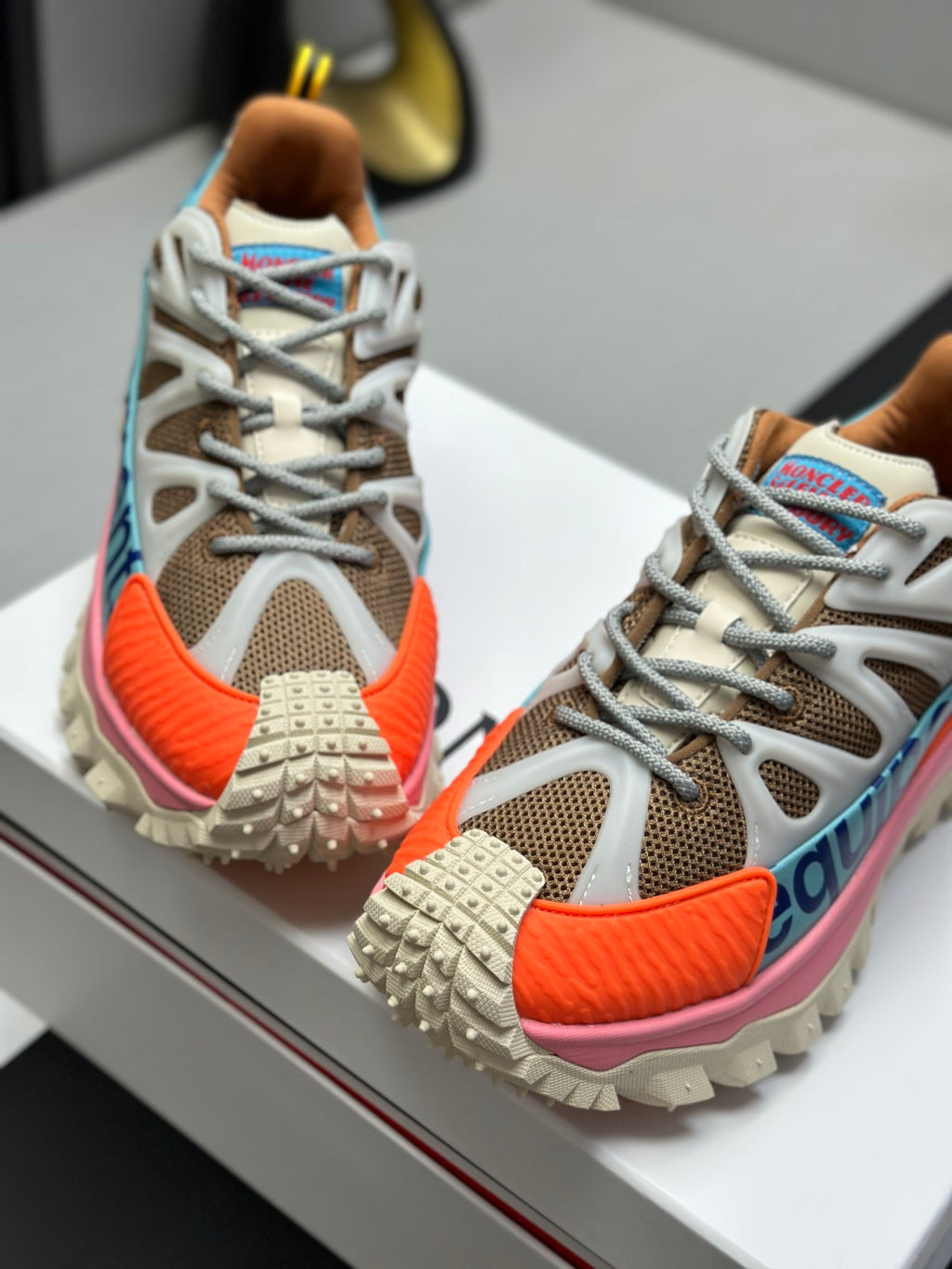 Moncler trail sneakers close-up, grey mesh, orange toe trim, white laces, blue accents
