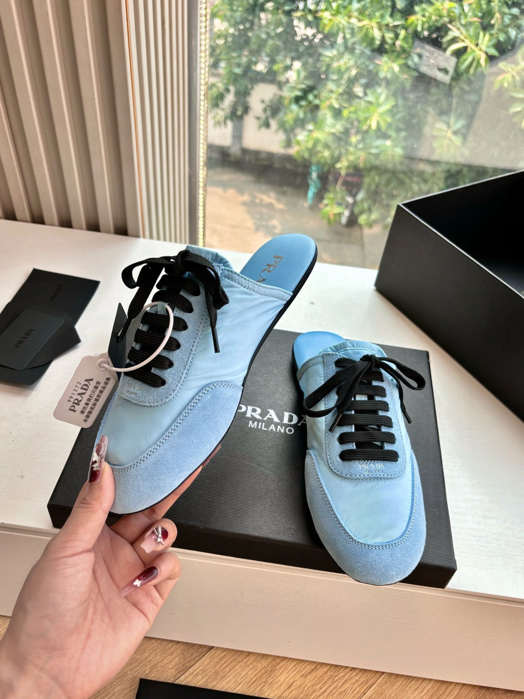 Prada women's light blue lace-up sneakers shown in hand, side profile with black laces