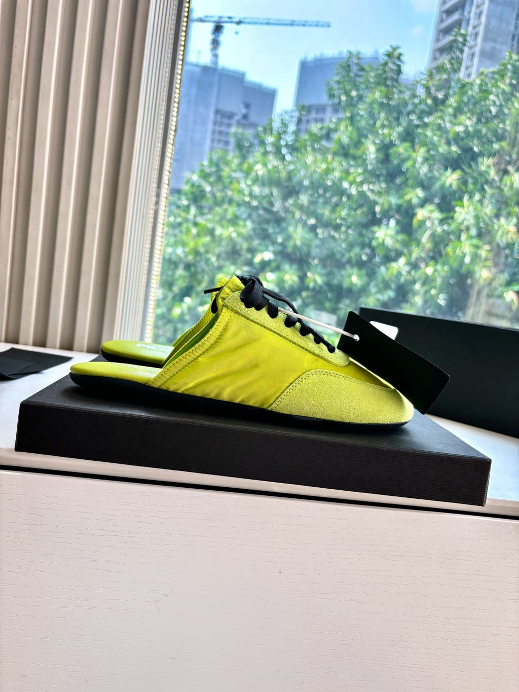 Neon yellow low-top sneaker with black laces, side view on black display base