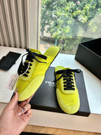Neon yellow lace-up sneaker held near box, black laces and Prada MILANO on side