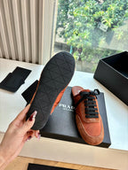 Prada low-top sneaker with tan suede upper, black laces, and treaded outsole