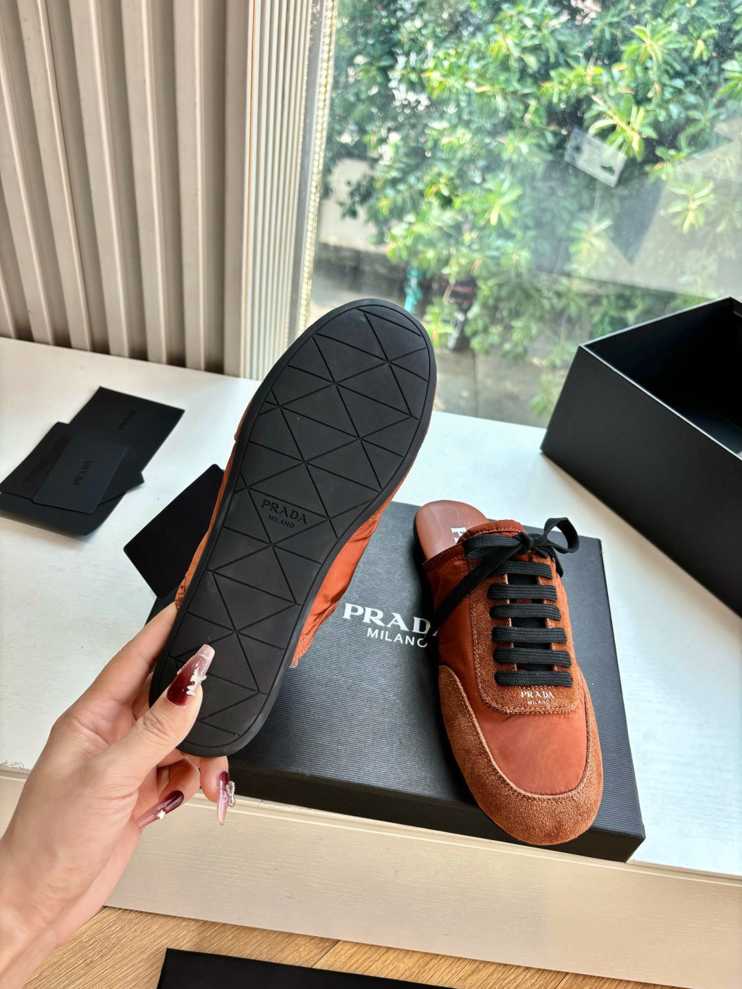 Prada low-top sneaker with tan suede upper, black laces, and treaded outsole