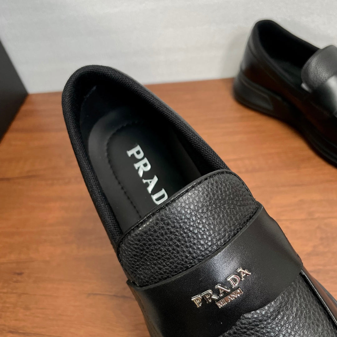 Prada unisex black loafer side view, featuring textured strap and gold PRADA logo