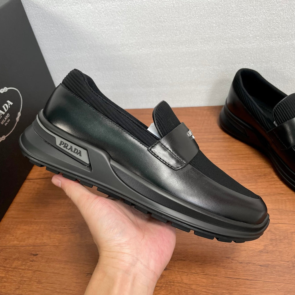 Prada unisex loafers shown in hand, black leather with metallic strap detail and chunky sole