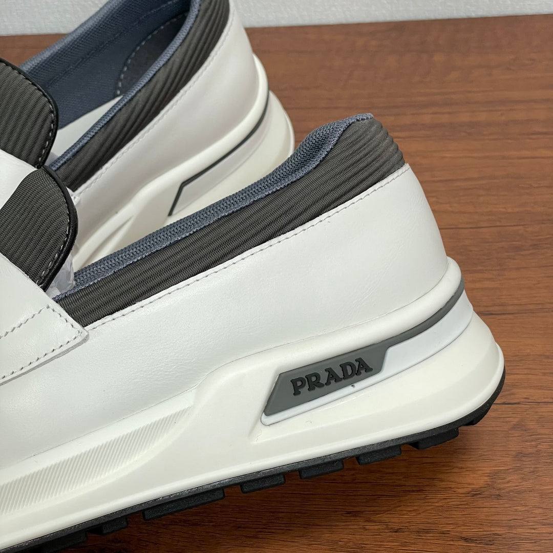 White slip-on sneaker side view with gray elastic band and Prada logo patch
