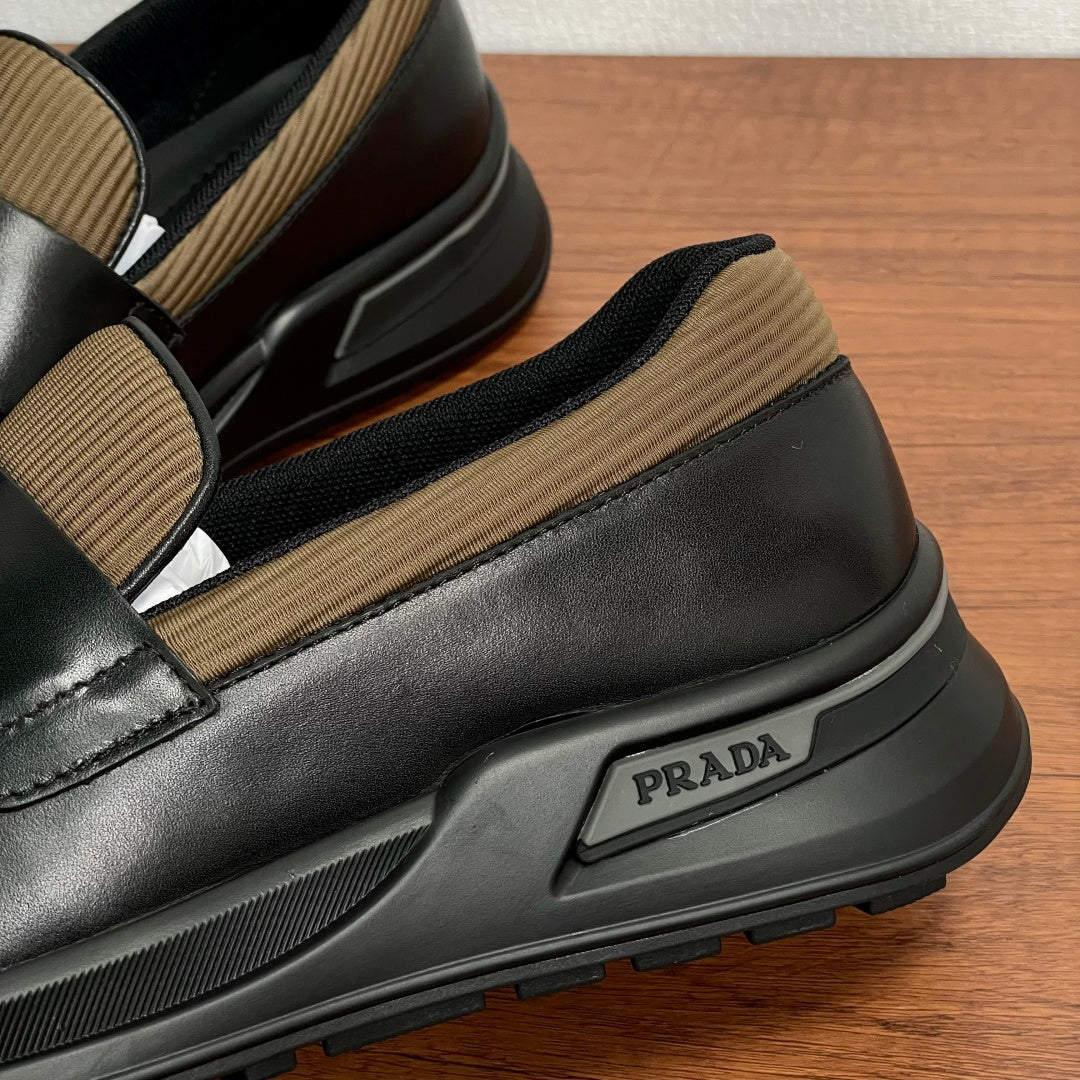 Prada unisex loafers close-up, black leather with tan knit strap and rubber midsole