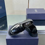 Black leather unisex loafers with strap buckle; side view and embossed footbed