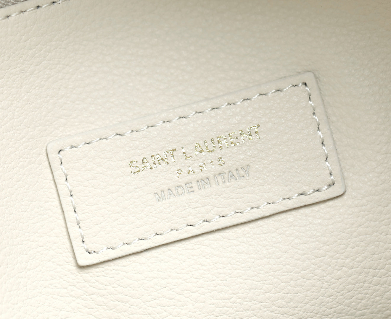 YSL bag white leather label with embossed branding and stitched border.