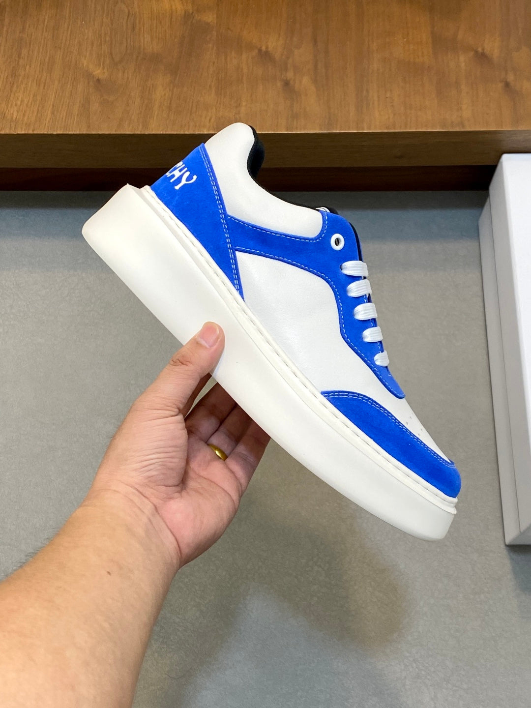 Blue and white low-top lace-up sneaker held in hand, side close-up