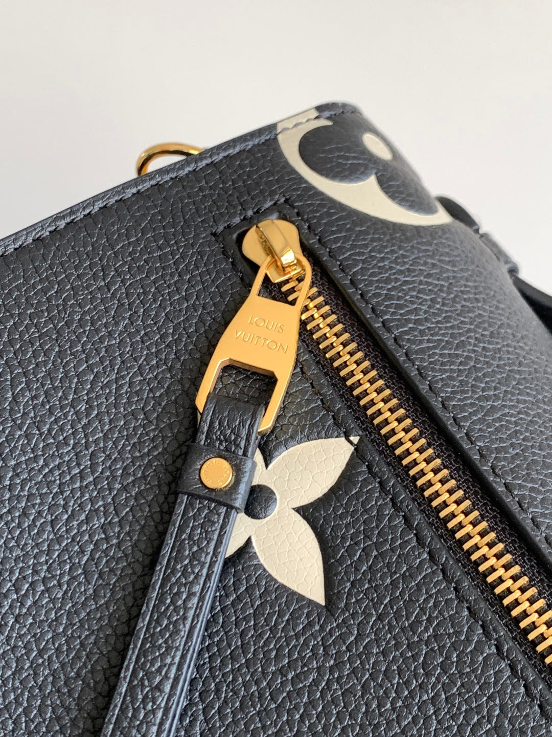 Louis Vuitton zipper pull and gold teeth on dark pebbled leather with monogram trim.