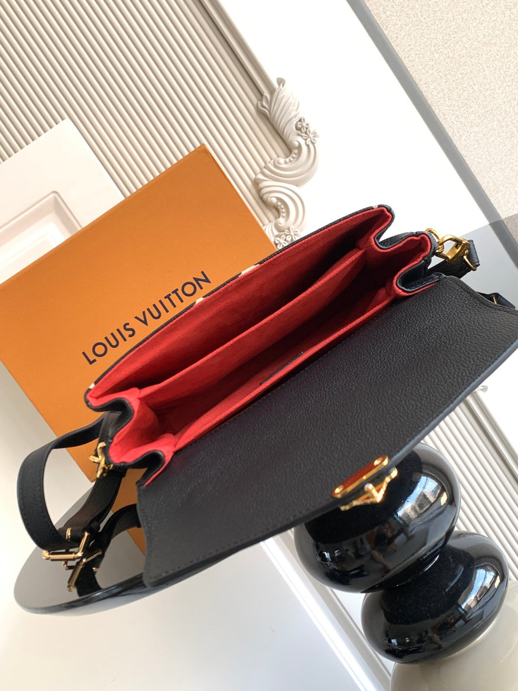 Louis Vuitton crossbody bag open to show red interior lining and dark exterior with gold hardware.