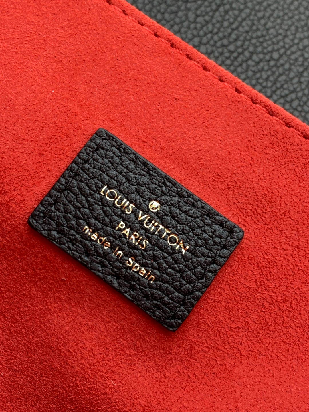 Louis Vuitton Paris made in Spain leather label card on red fabric background.