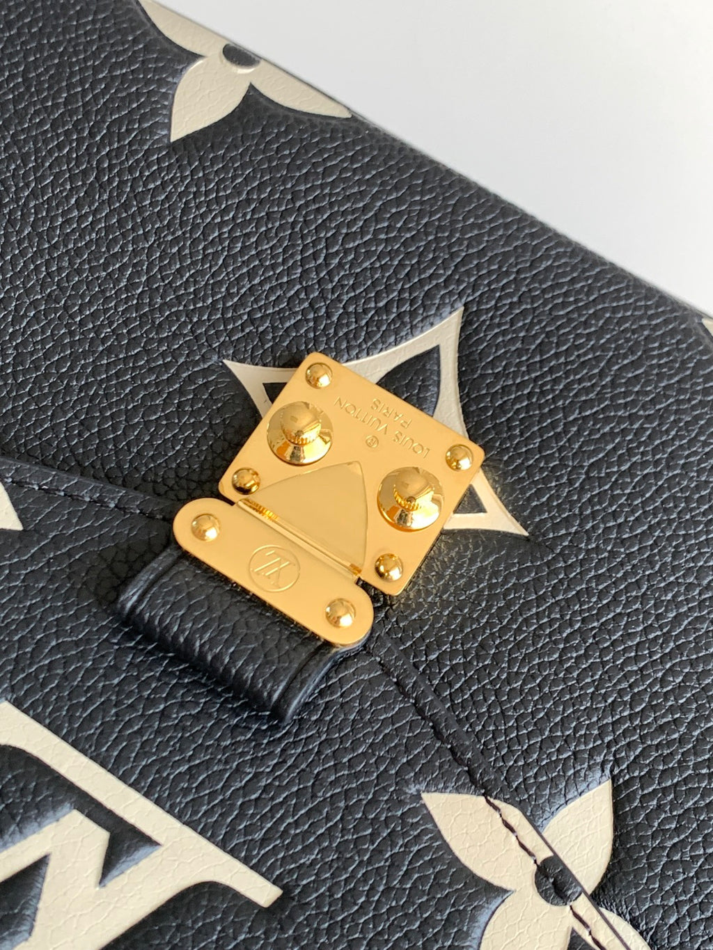 Louis Vuitton flap clasp detail on dark pebbled leather with gold hardware and monogram accents.