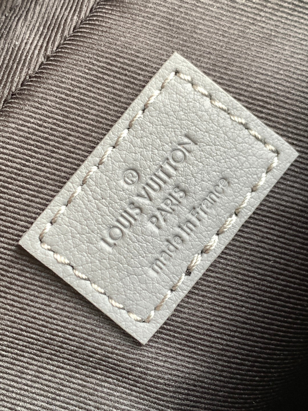 Louis Vuitton logo patch on gray fabric, stitched label detail.