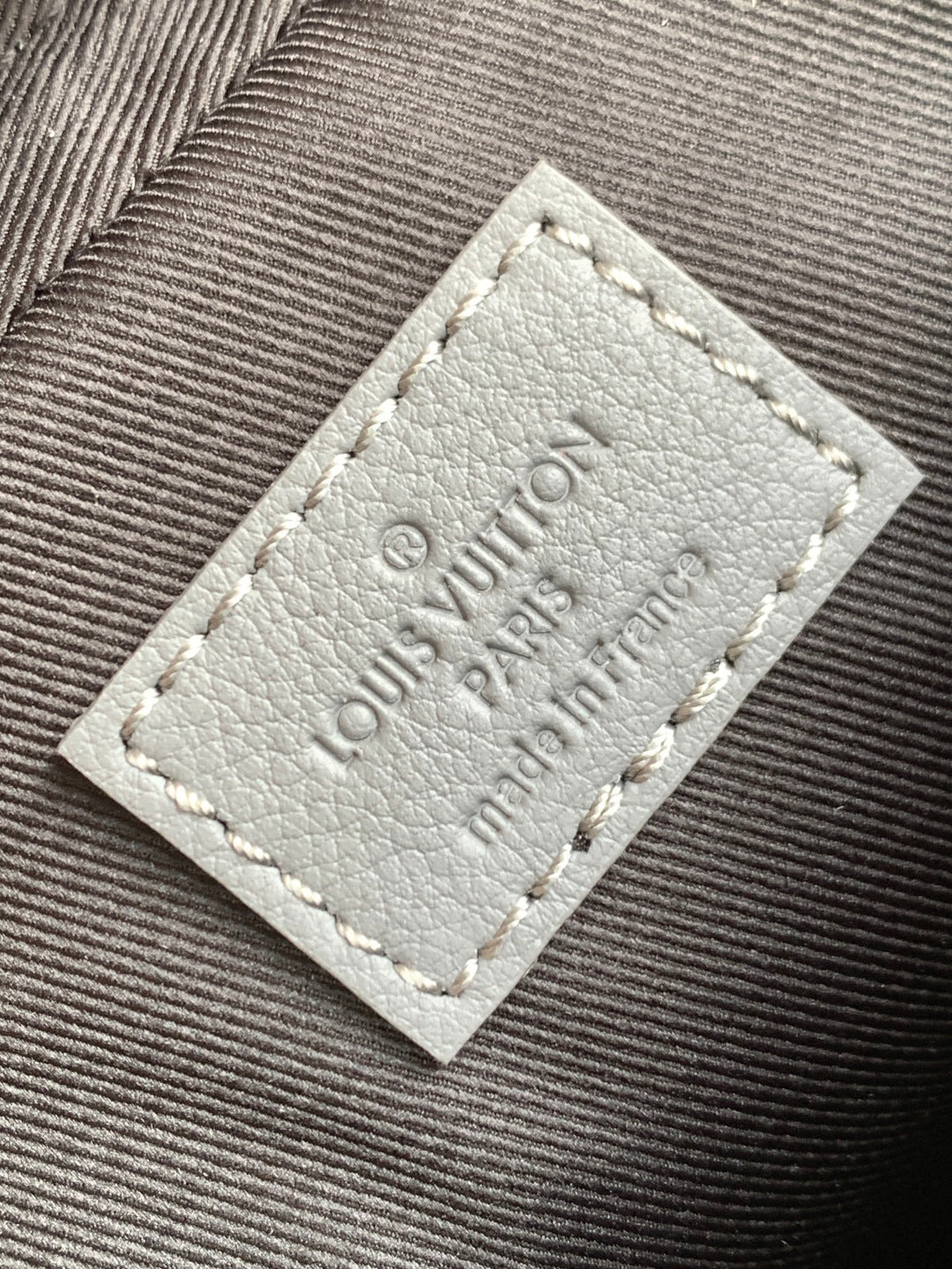 Louis Vuitton logo patch on gray fabric, stitched label detail.