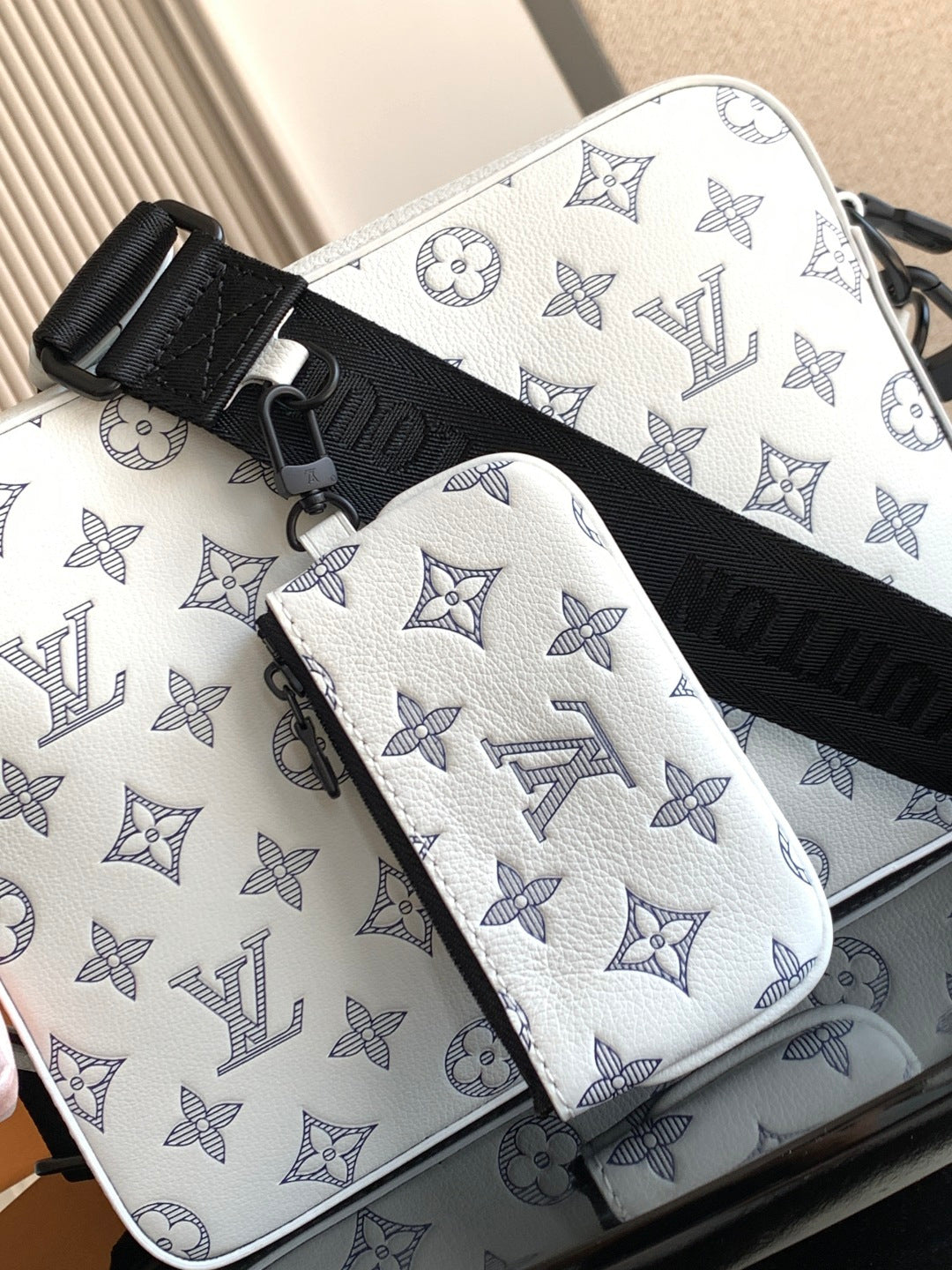 Crossbody bag with white base and light blue monogram, black crossbody strap