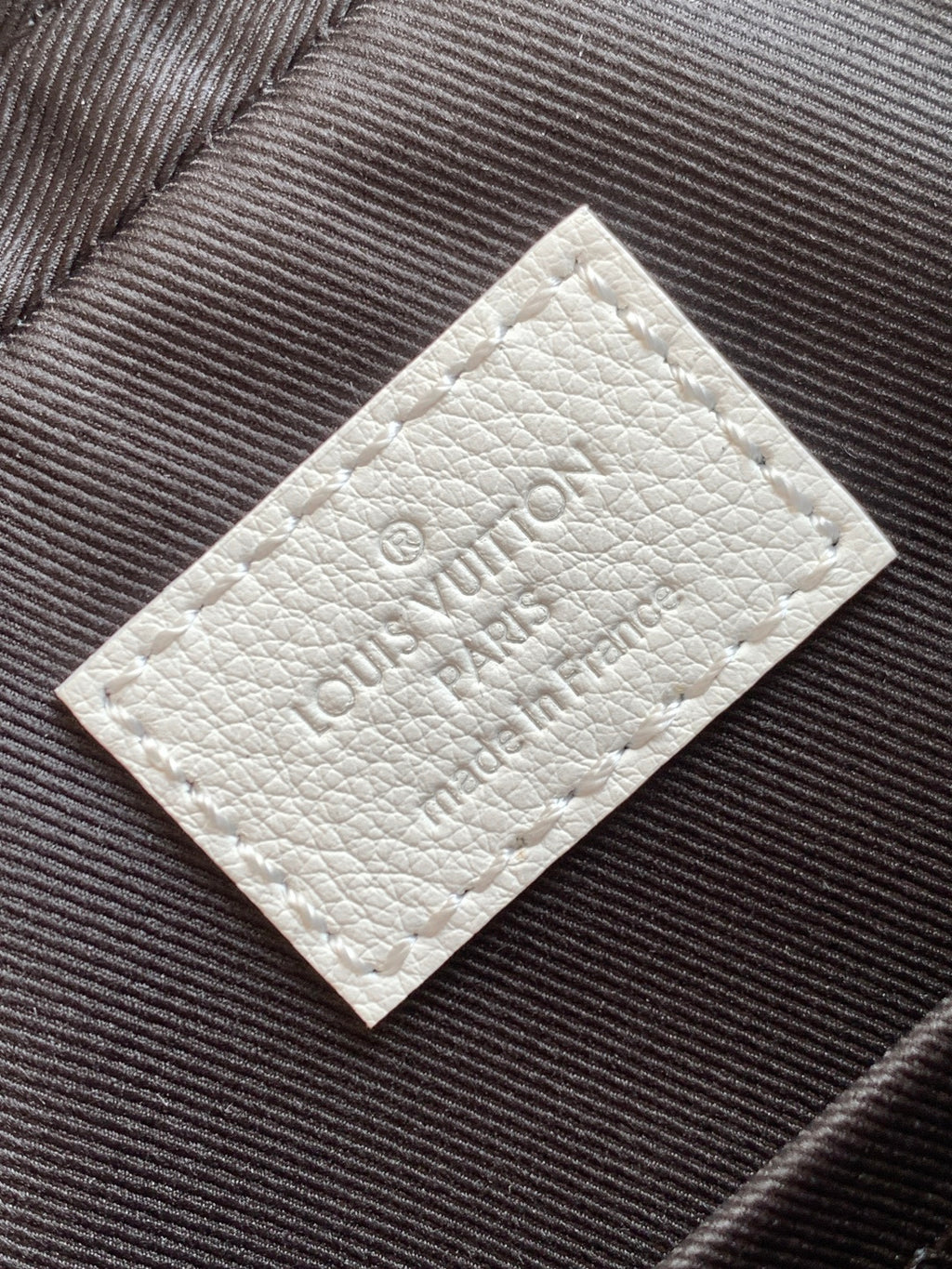 White leather logo patch with embossed Louis Vuitton lettering