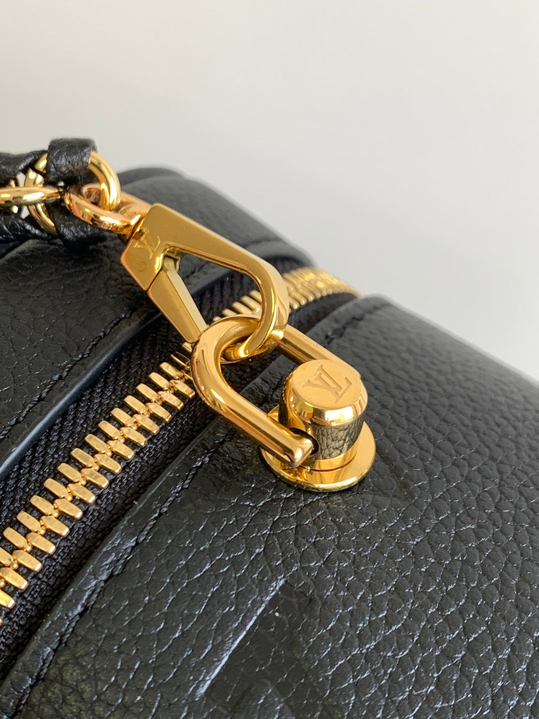 Gold clasp and chain detail on black Louis Vuitton monogram bag zipper