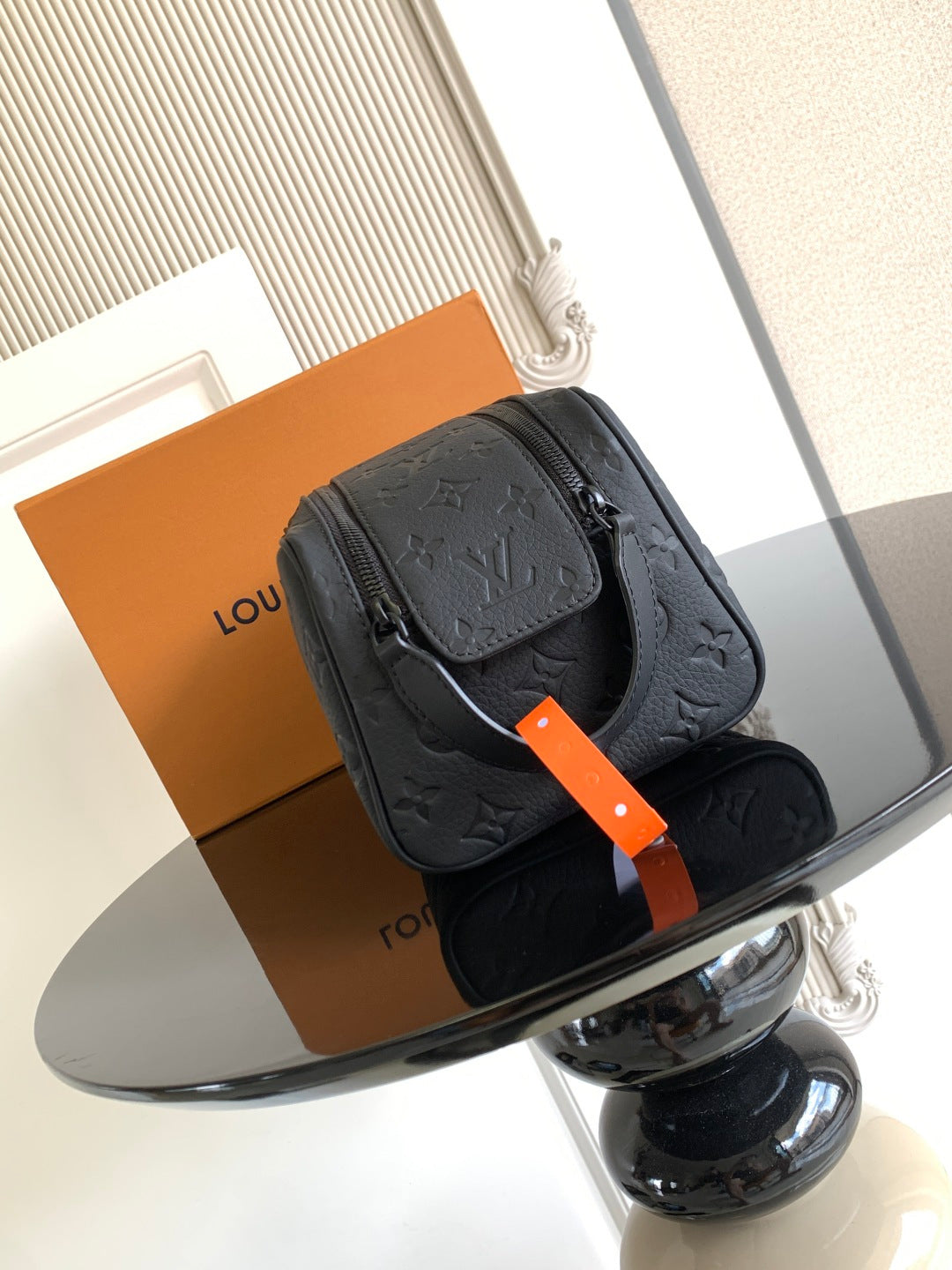 Louis Vuitton bag with dark monogram texture, top zipper, and orange tag