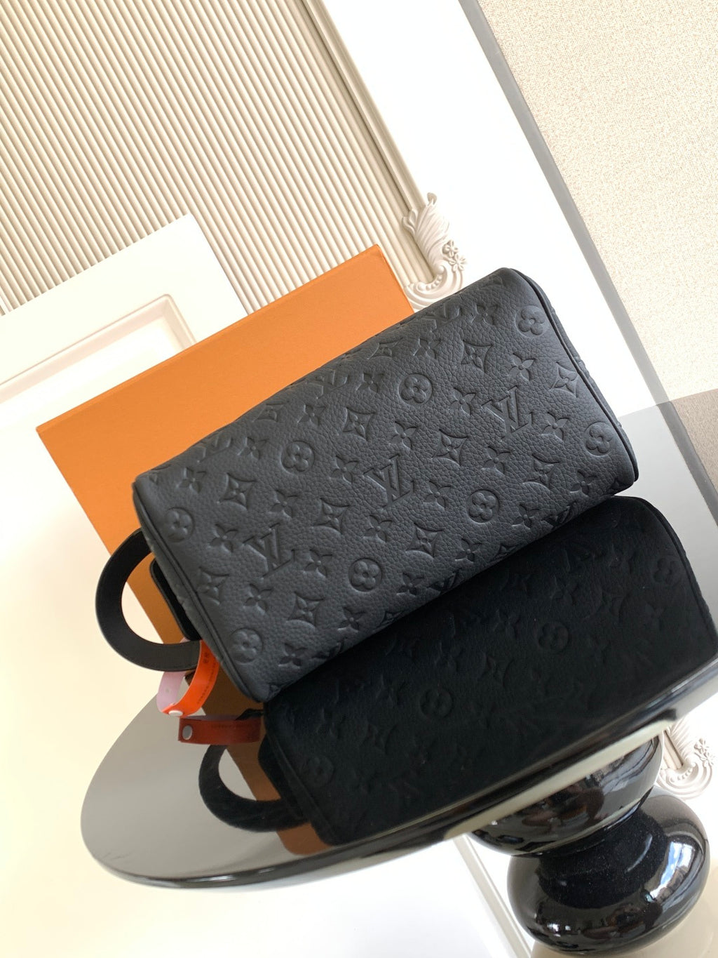 Louis Vuitton bag with dark monogram texture, ring strap, and orange hanging tag