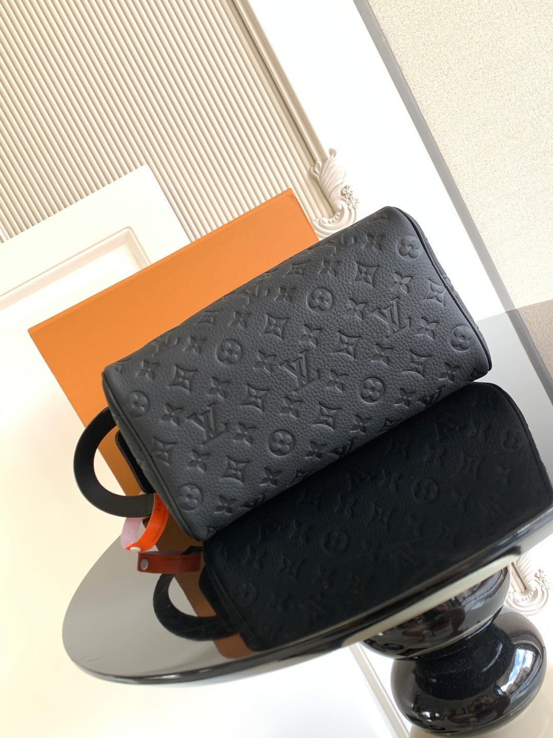 Louis Vuitton bag with dark monogram texture, ring strap, and orange hanging tag