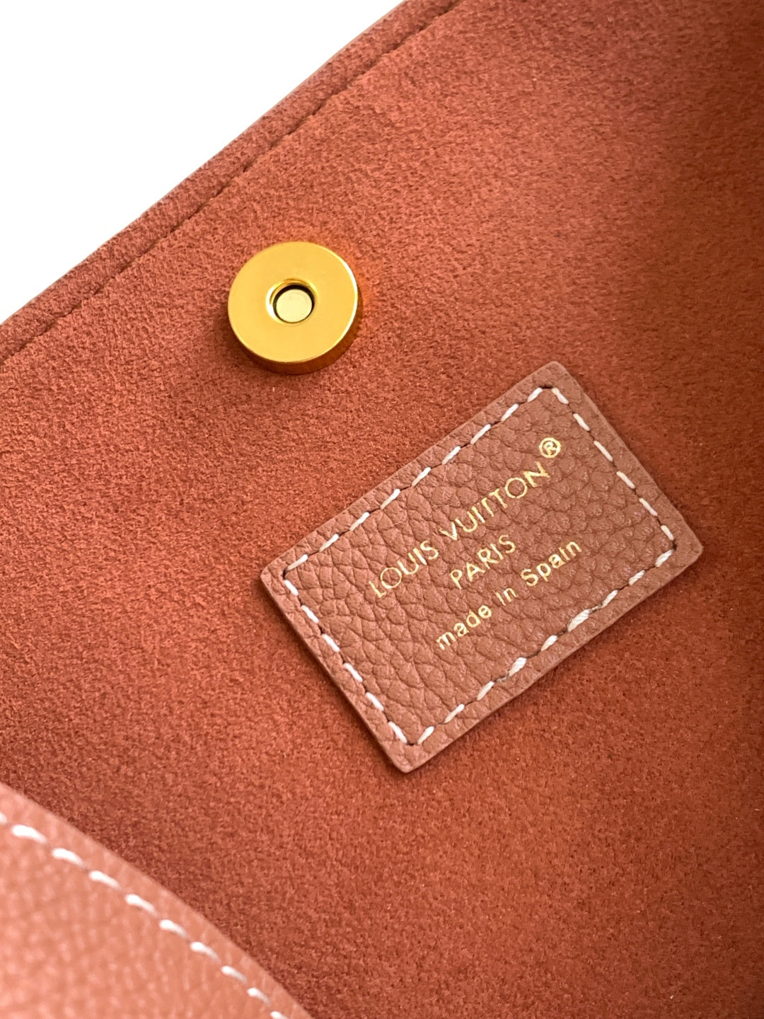 Louis Vuitton leather bag snap and small logo label patch on pink textured surface