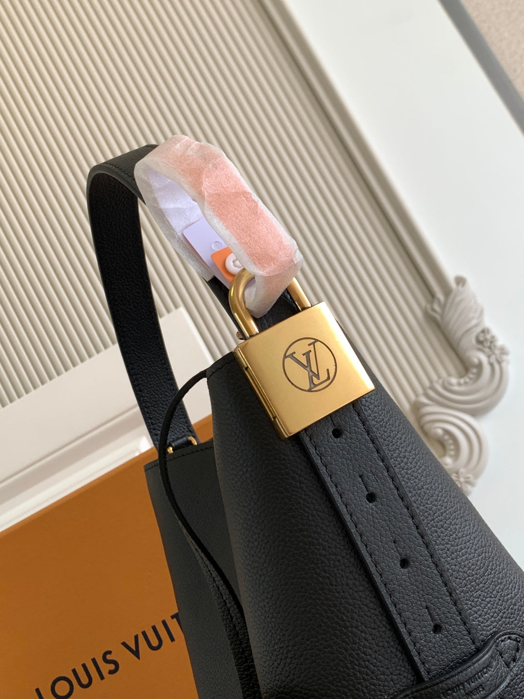 Black leather handbag handle with gold charm lock and black shoulder strap.