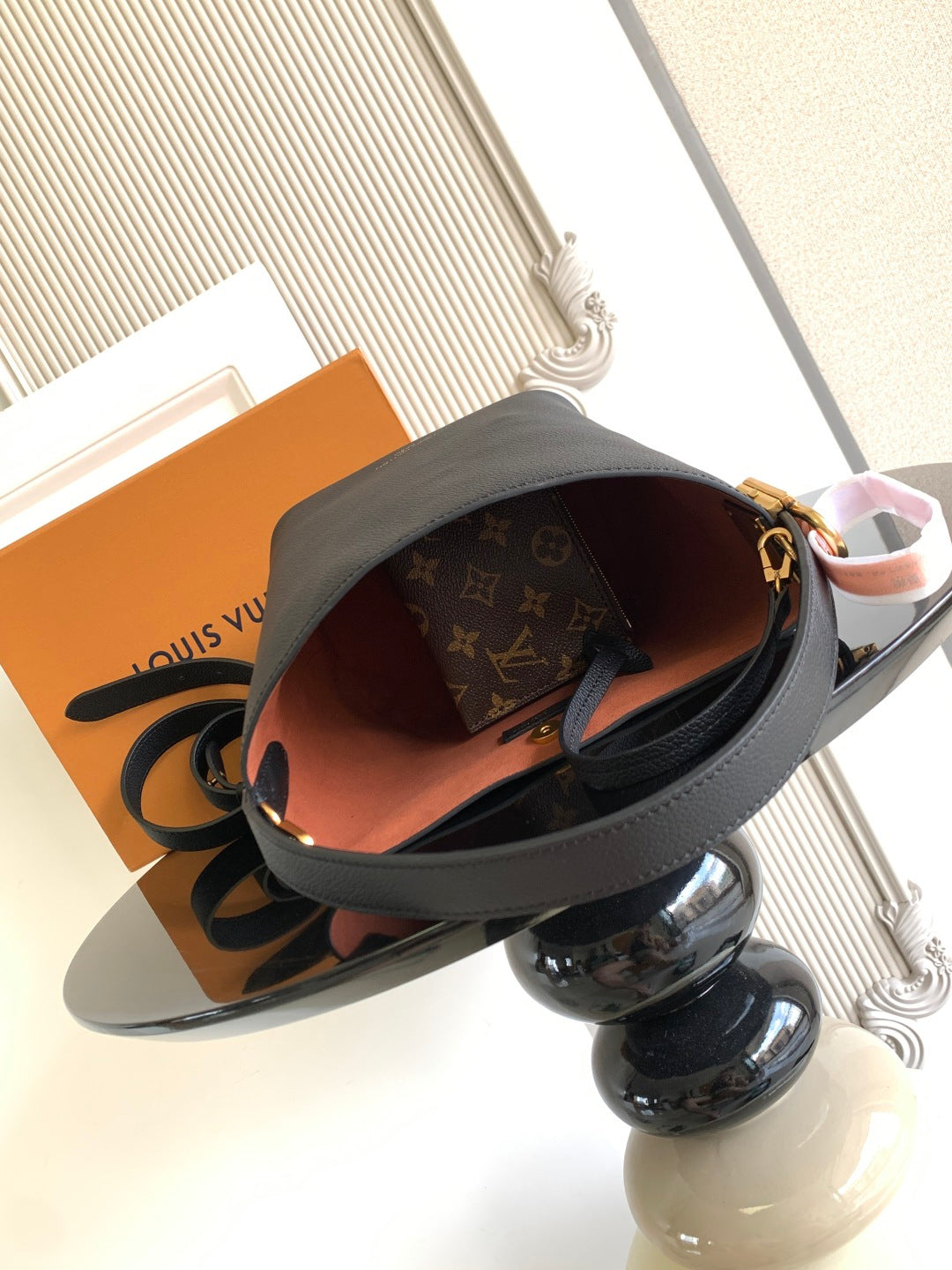 Black leather bucket bag open to reveal brown monogram lining and interior.