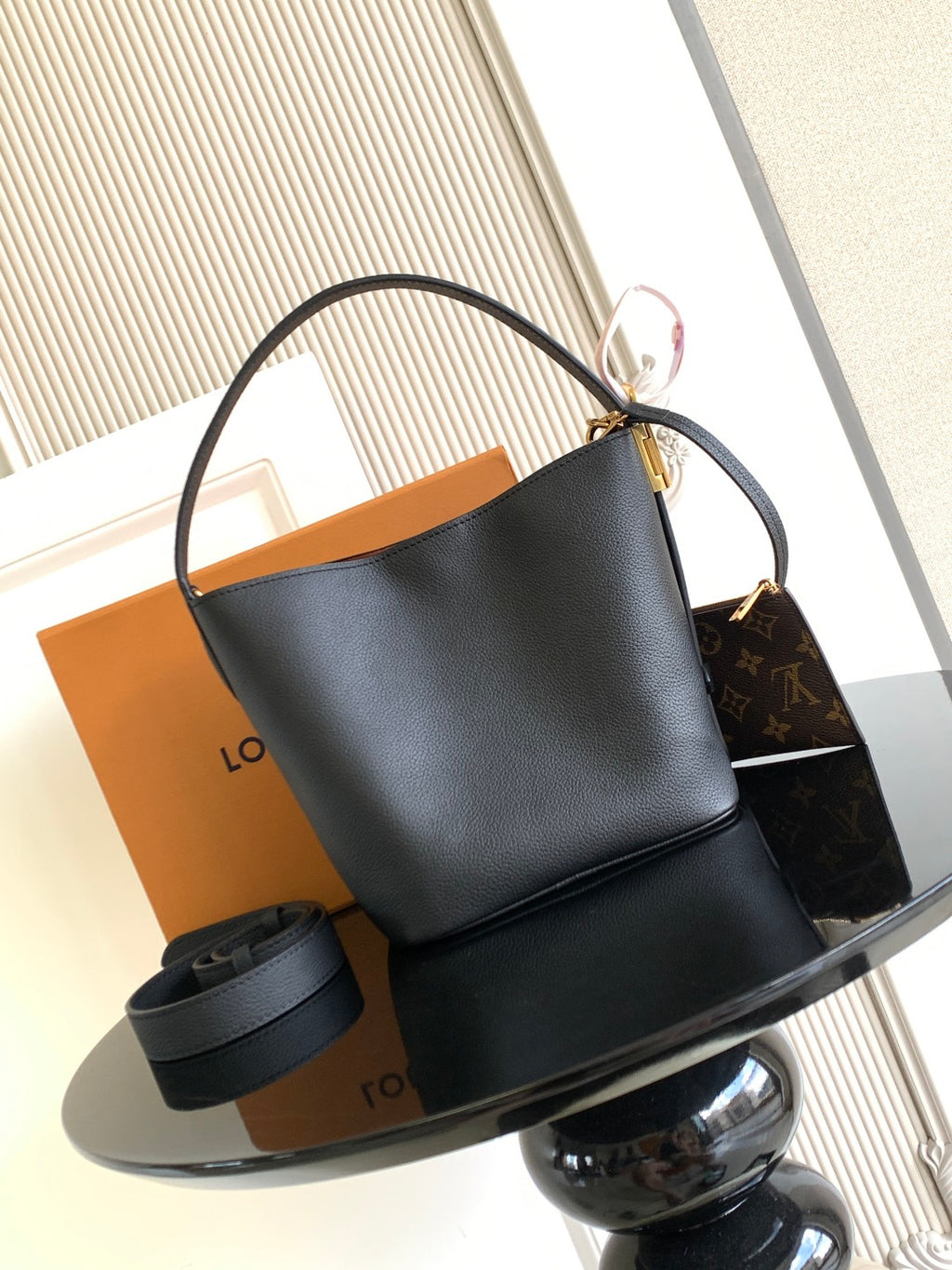 Black leather bucket bag with curved top handle and open interior, gold hardware.