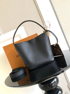 Black leather bucket bag with curved top handle and open interior, gold hardware.