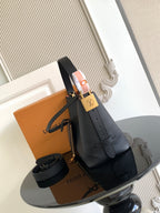Black leather bucket bag with shoulder strap and gold-tone hardware, compact design.