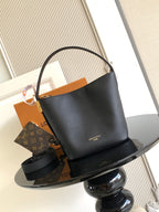 Black leather bucket bag with top handle and gold-tone hardware, open top.