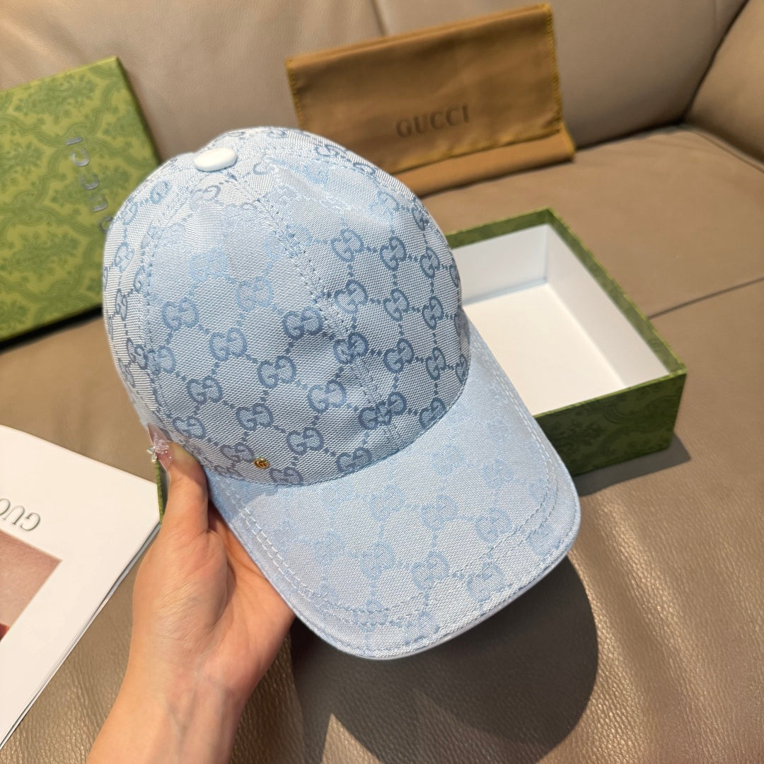 Gucci cap in light blue GG monogram pattern with curved brim, held in a hand.